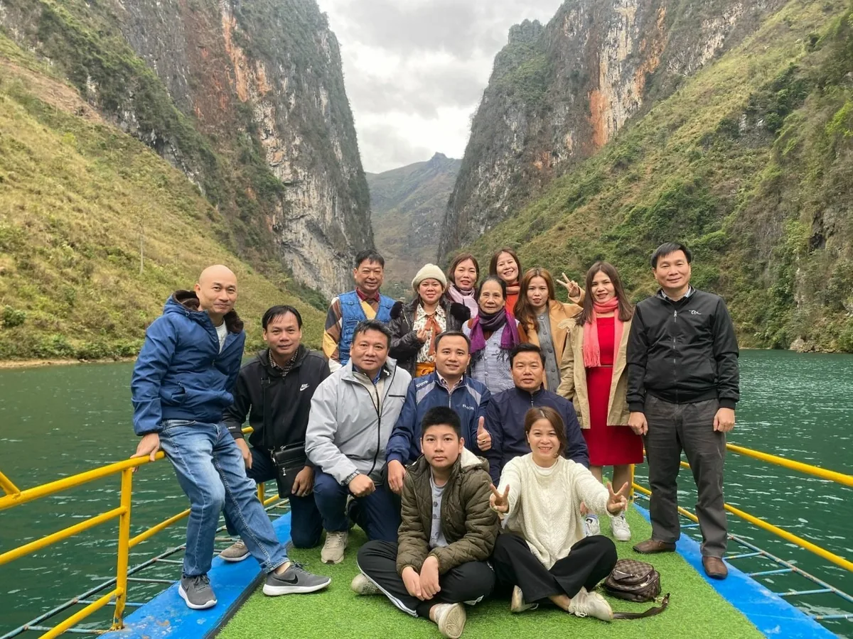 A group of tourists poses on a boat deck cruising through the towering limestone gorge of Nho Que River in Ha Giang.
