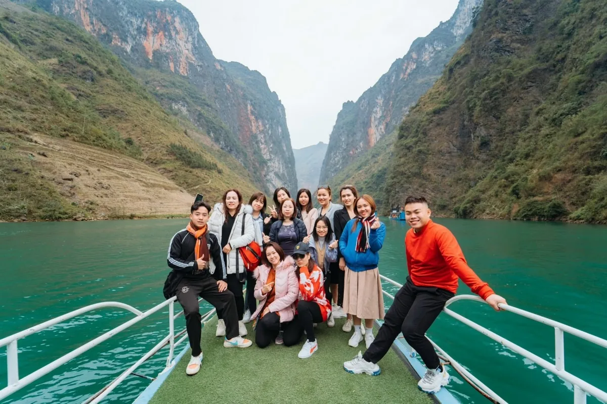 A group of tourists pose on a boat gliding through the turquoise waters of the Nho Que River canyon in Ha Giang.