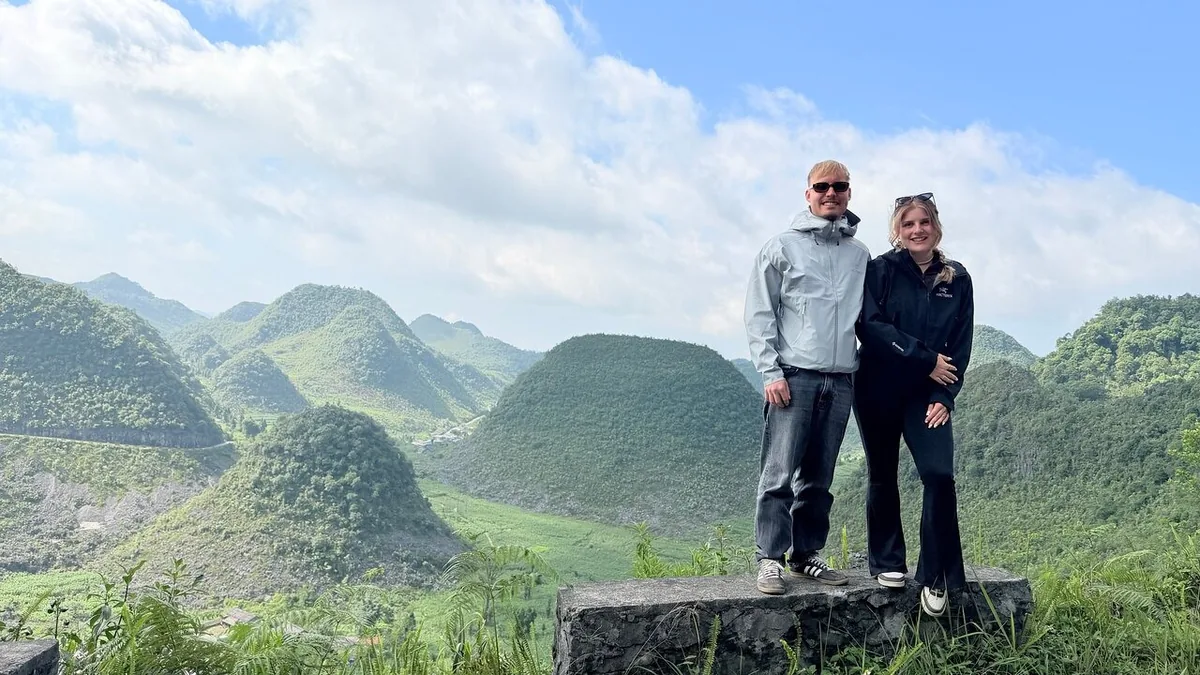 A couple stands on a stone platform overlooking the cone-shaped karst mountains along the Ha Giang Loop.