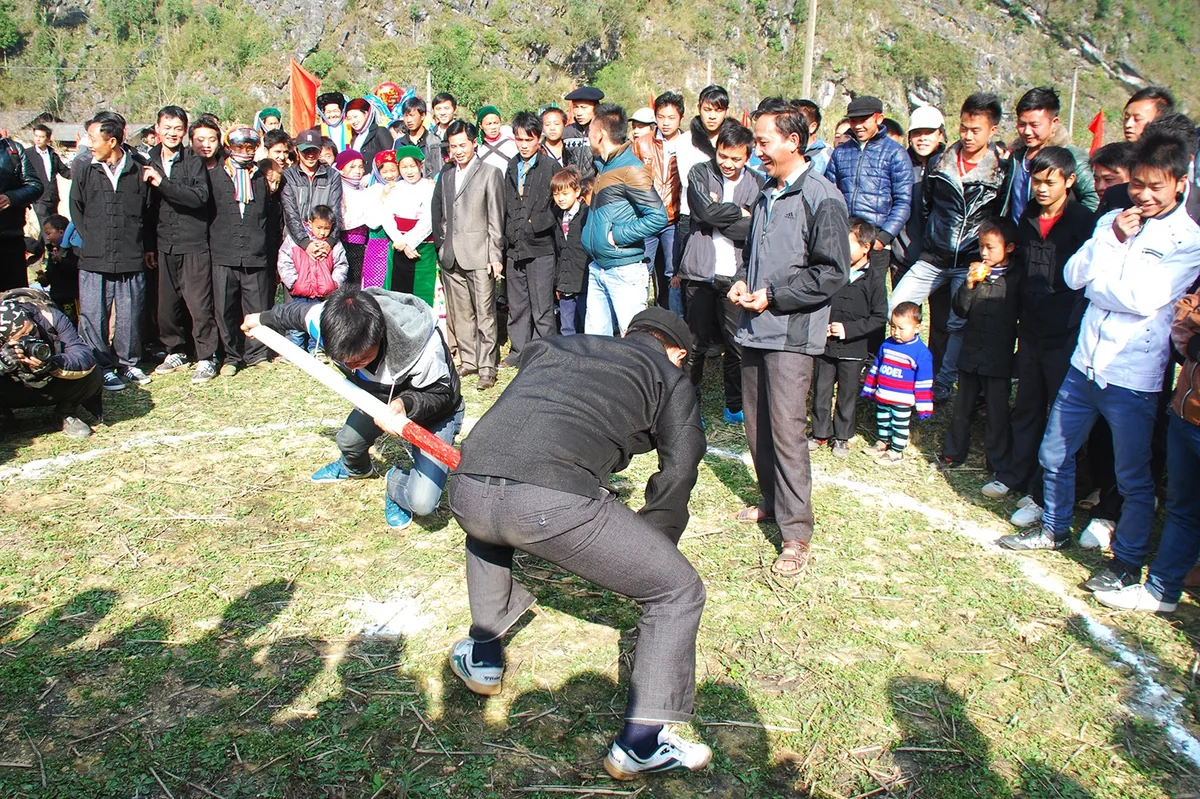 A crowd watches two men wrestling with a wooden pole inside a chalk circle at a Ha Giang festival.