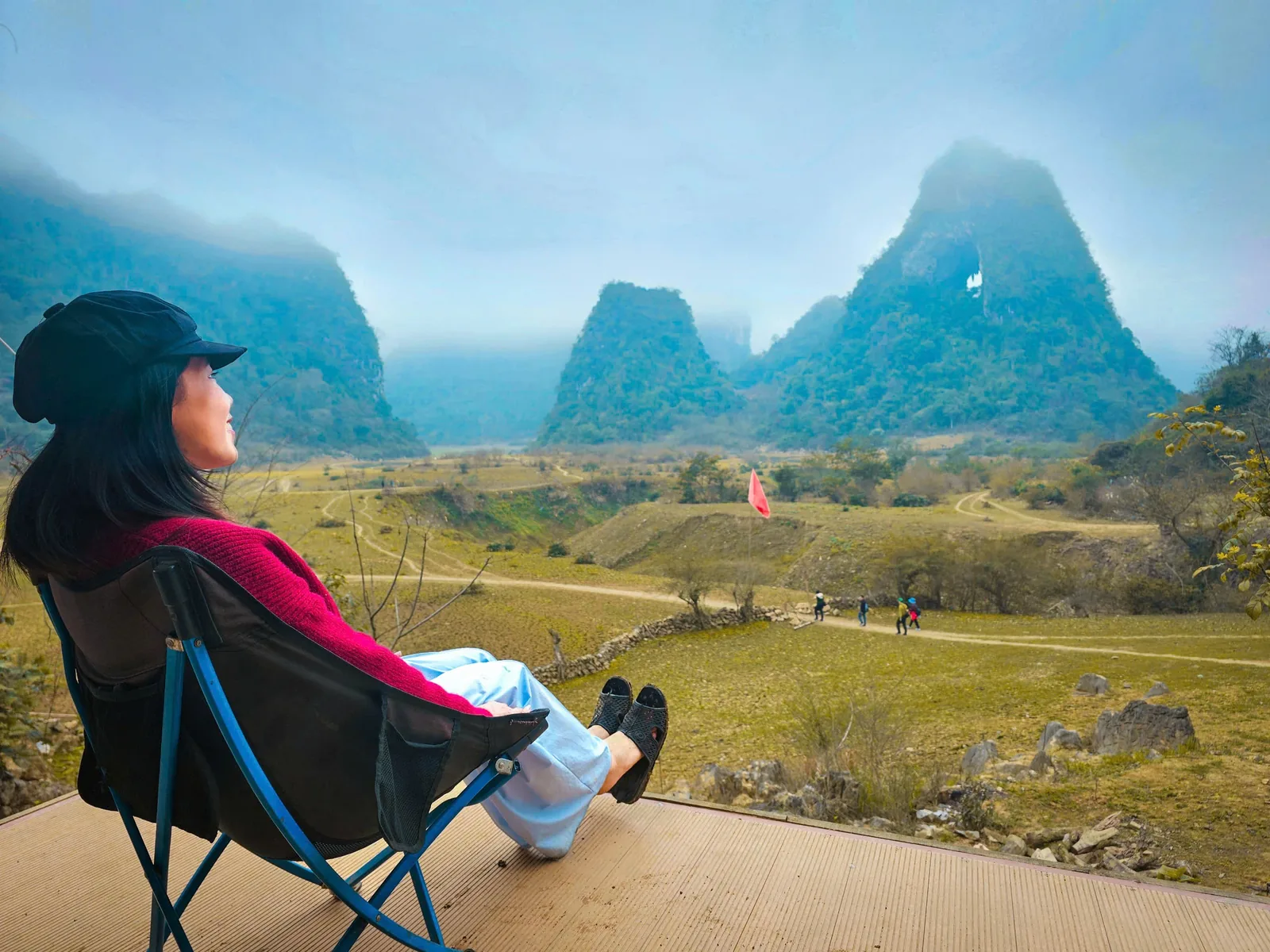 A woman relaxes in a camping chair overlooking limestone karst mountains and a green valley in Cao Bang.