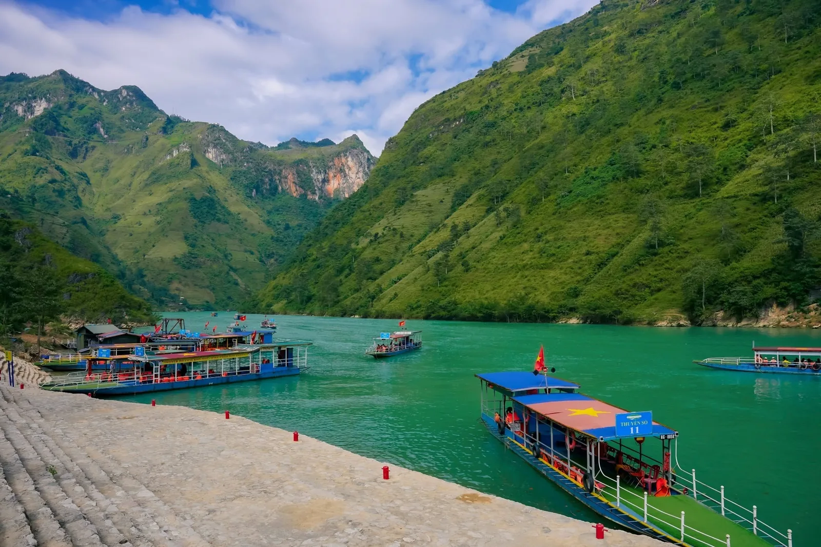 Colorful boats float on turquoise water between steep green mountains at Ha Giang's Nho Que River in Vietnam.