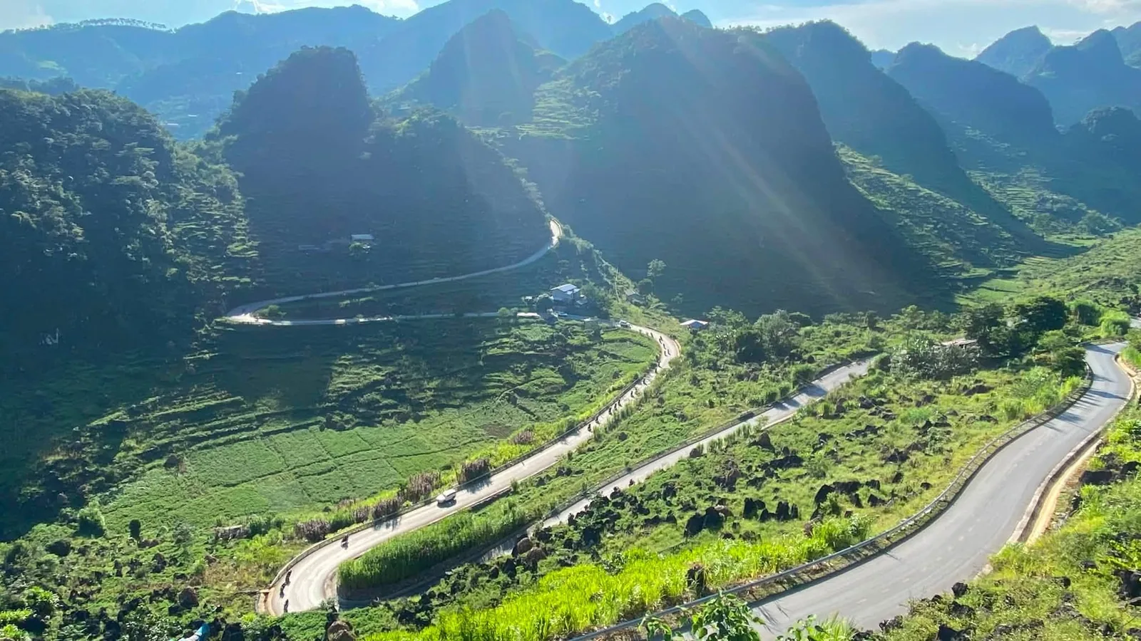 A winding mountain road snakes through green valleys and karst peaks in Ha Giang.