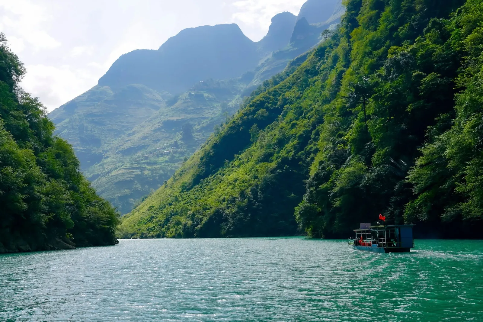 A small boat cruises along the turquoise river through steep, forested limestone mountains near Ha Giang.