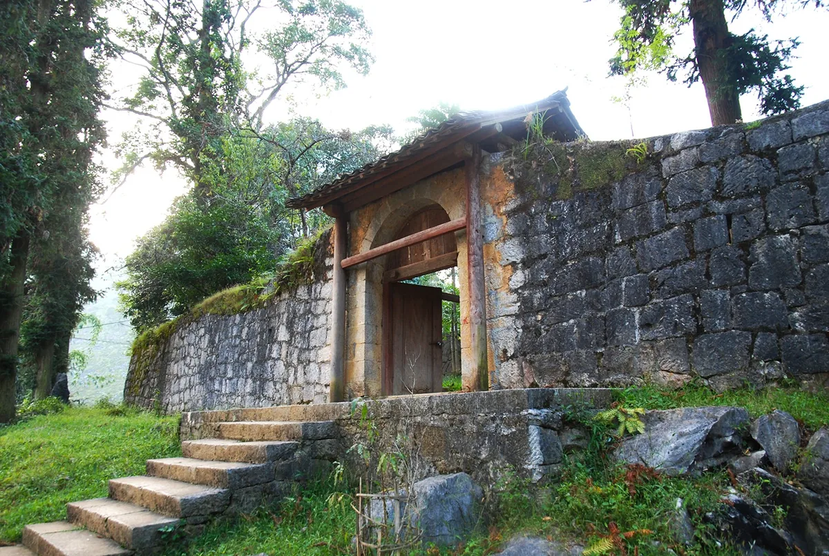 A stone gate with wooden door and tiled roof leads into the old Hmong King's Palace grounds in Ha Giang.