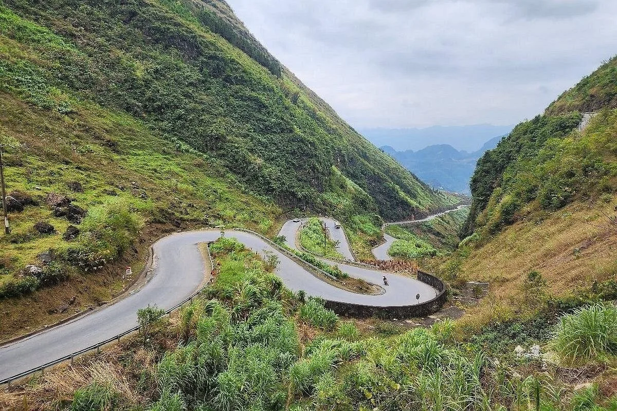 A winding switchback road curves through green mountains on the Ha Giang Loop in Vietnam.