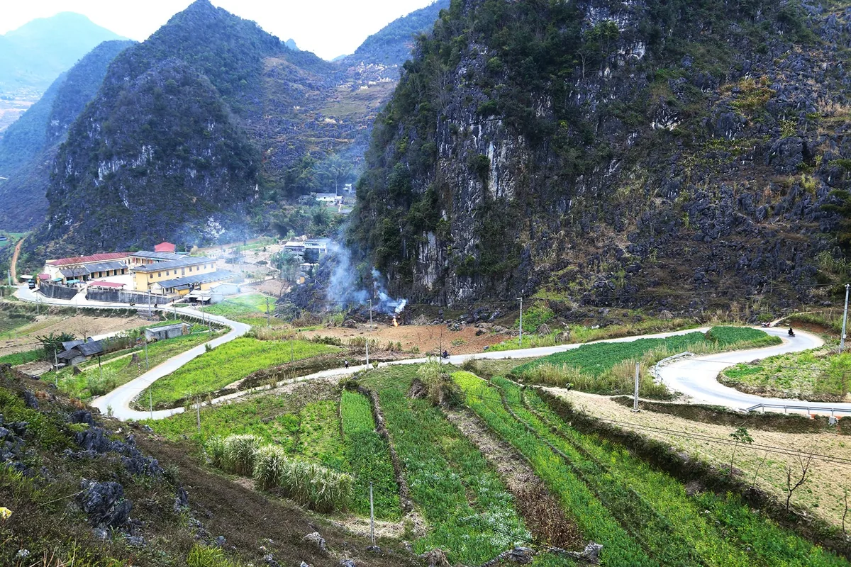 A winding mountain road cuts through green terraced fields beside limestone karsts in Ha Giang.